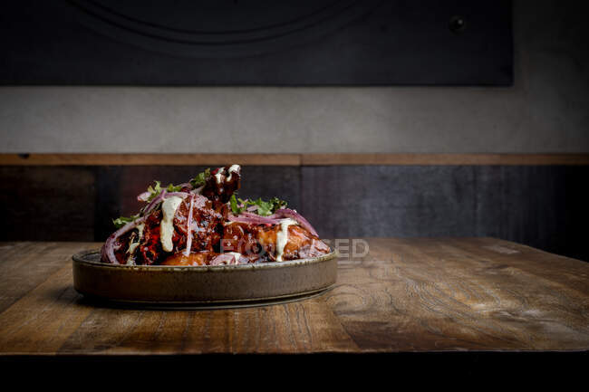 Gustose ali di pollo alla griglia con salsa barbecue e cipolla servite sul piatto sul tavolo di legno nel ristorante — Foto stock
