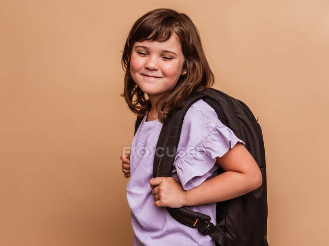 Cute schoolchild standing on brown background in studio and closed eyes — Stock Photo