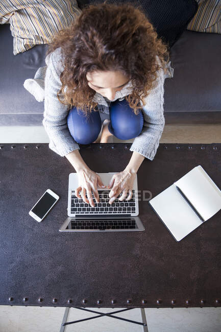 Draufsicht einer Geschäftsfrau mit lockigem Haar, die auf dem Sofa sitzt und mit ihrem Laptop arbeitet — Stockfoto