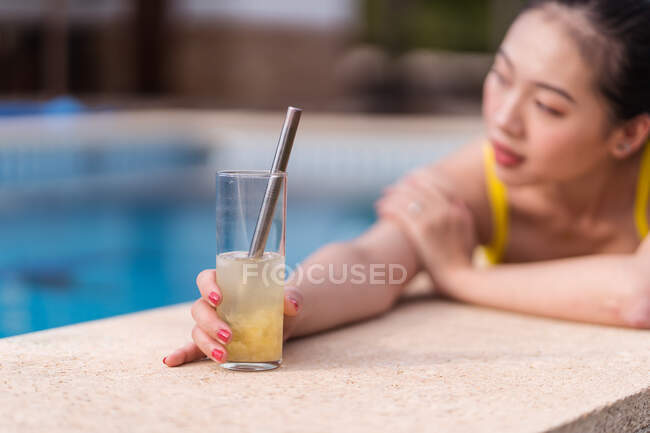 Vue latérale de la femelle asiatique en bikini jaune située près de la piscine et bronzer tout en profitant des vacances d'été en station balnéaire — Photo de stock