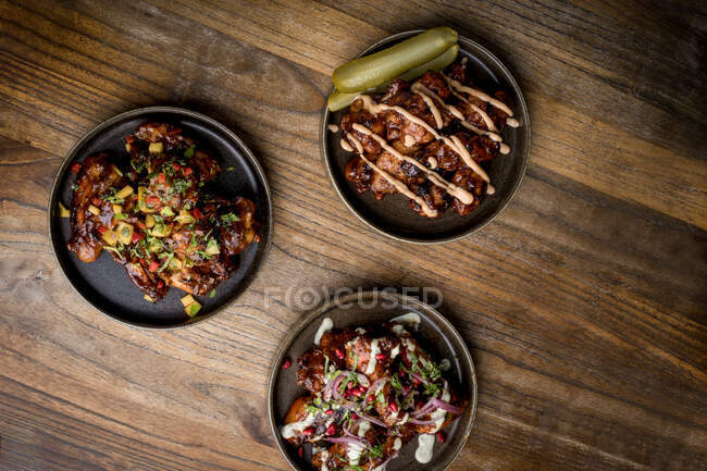 Set of delicious grilled chicken wings in BBQ sauce served with vegetables on round plates and placed on wooden table in restaurant — Stock Photo