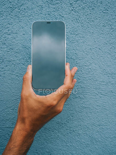 Crop unrecognizable male showing modern mobile phone with black screen on blue background in city — Stock Photo