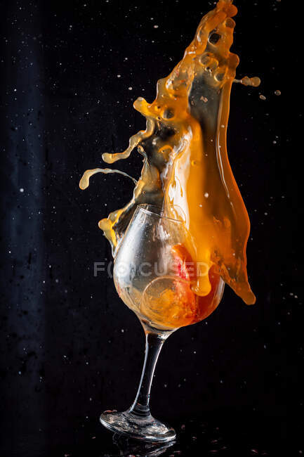 Холодний алкоголь апельсиновий напій виливається зі скляної чаші на чорному фоні в студії — стокове фото