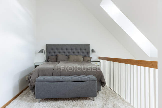 Удобная кровать с серой постельное белье помещается на мягком белом ковре в маленькой спальне в минимальном стиле в доме — стоковое фото