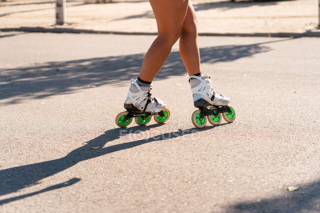 Cropped unrecognizable fit female in rollerblades showing stunt on road in city in summer — Stock Photo