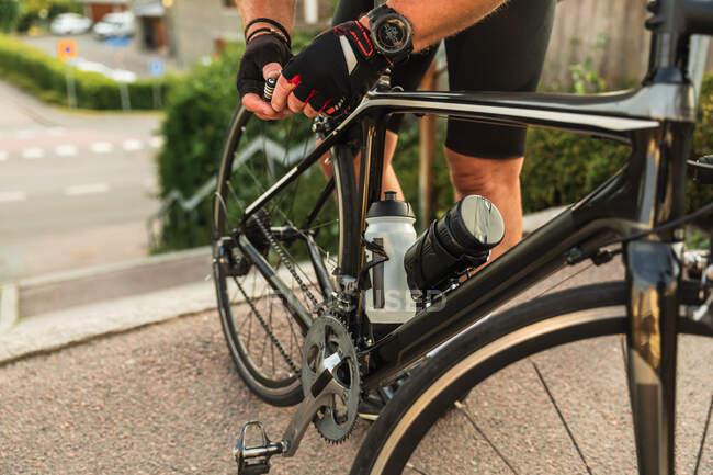 Crop anonymous male biker fixing bicycle tire on road while preparing for workout in town — Stock Photo
