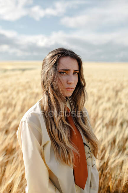 Young mindful female in formal wear with tie looking at camera among spikes in countryside — Stock Photo