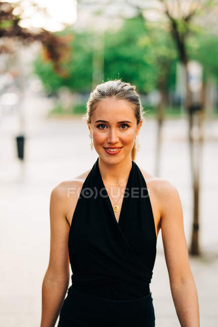 Femme positive dans des vêtements élégants debout n rue de la ville et regardant la caméra — Photo de stock