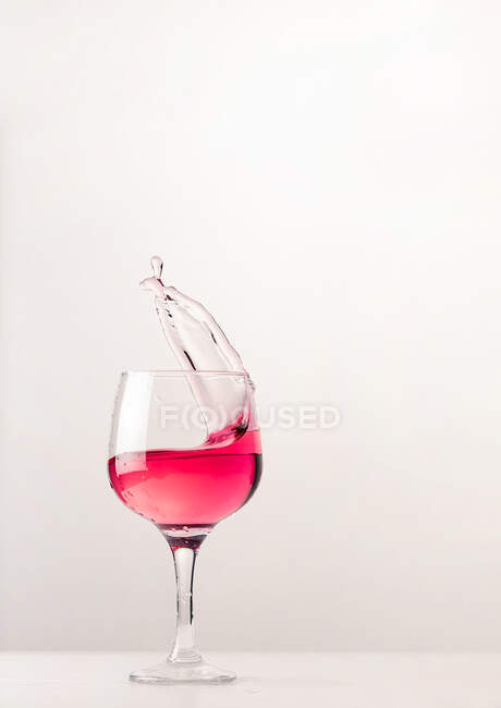 Cristal vidro brilhante com álcool rosa salpicando coquetel no fundo branco no estúdio — Fotografia de Stock