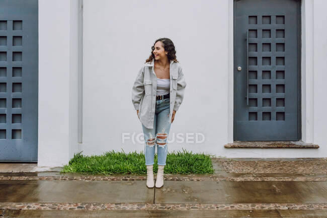 Mulher encantada em roupas da moda entre duas portas do edifício residencial e desfrutando de tempo chuvoso na cidade — Fotografia de Stock