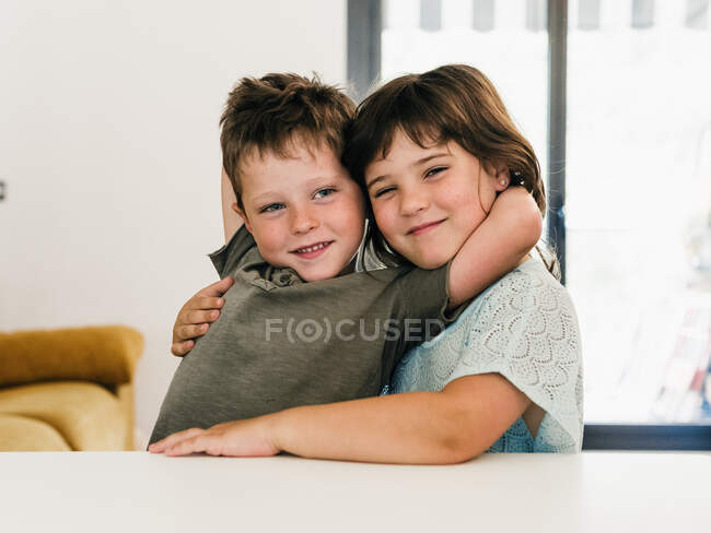Nette zufriedene Zwillinge umarmen sich zärtlich und sitzen zu Hause im Wohnzimmer zusammen und schauen in die Kamera — Stockfoto