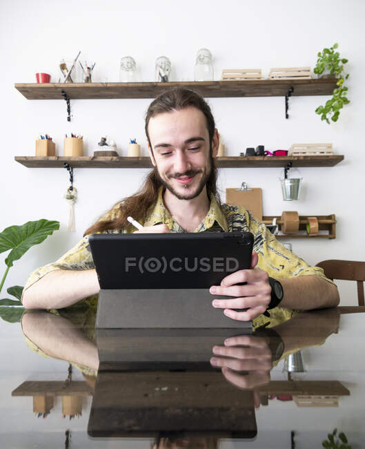 Diseño masculino de contenido dibujado en una tableta gráfica con lápiz óptico mientras está sentado en la mesa en un estudio creativo y trabajando en un proyecto - foto de stock