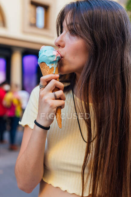 Cultiver jeune femelle lécher savoureux gelato dans un cône de gaufre en ville sur fond flou — Photo de stock