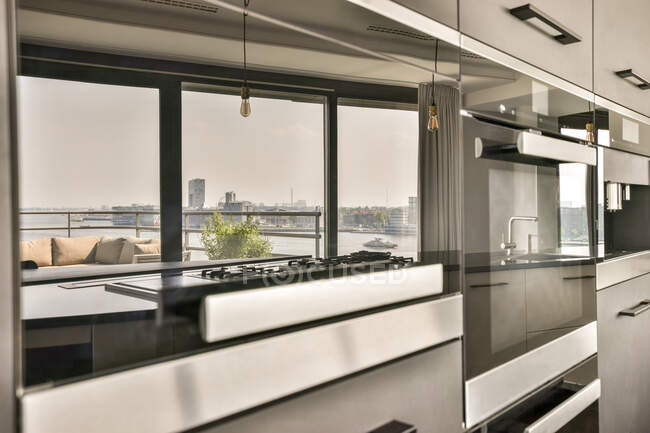 Фрагмент дизайну інтер'єру сучасної домашньої кухні в стилі лофт з вбудованою плитою і шафами перед вікном з видом на міський пейзаж з каналом — стокове фото