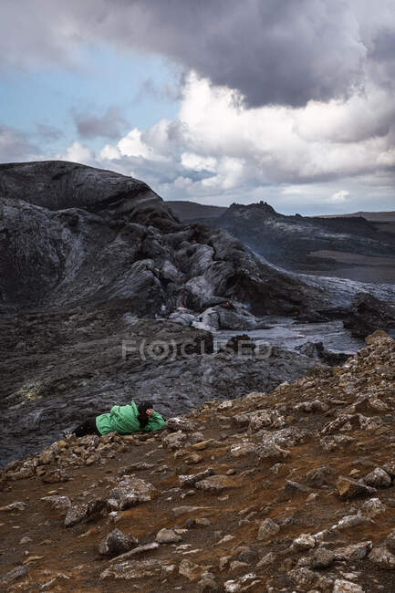 Обратный вид на неузнаваемого путешественника, лежащего на горе и созерцающего Федрадальсфьолл в Исландии — стоковое фото