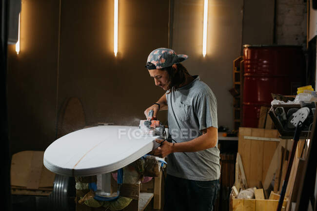Shaper masculino usando plaina elétrica e superfície de polimento de prancha de surf na oficina — Fotografia de Stock