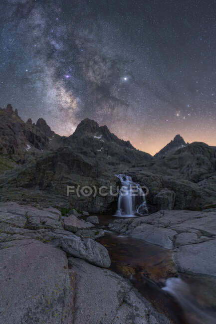 Spektakulärer Blick auf hohe raue Berge mit Kaskade und Fluss unter Sternenhimmel mit Galaxie am Abend — Stockfoto