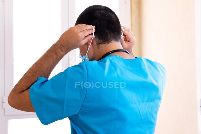 Rückenansicht eines männlichen Arztes, der sich während seiner Arbeit in der Klinik eine schützende Gesichtsmaske aufsetzt — Stockfoto