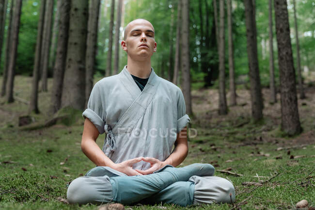 Лиса людина в традиційному одязі сидить на траві в позі Лотоса і медитує під час тренування кунг-фу в лісі. — стокове фото