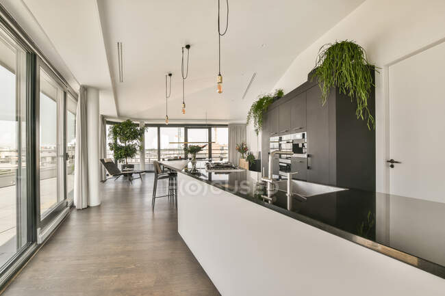 Table à manger et chaises placées près de la cuisine ouverte dans un appartement moderne de style loft avec murs blancs et plafond dans un appartement spacieux — Photo de stock