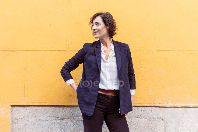 Самозабезпечена елегантна жінка в офіційному вбранні, що стоїть з руками на талії і дивиться — стокове фото