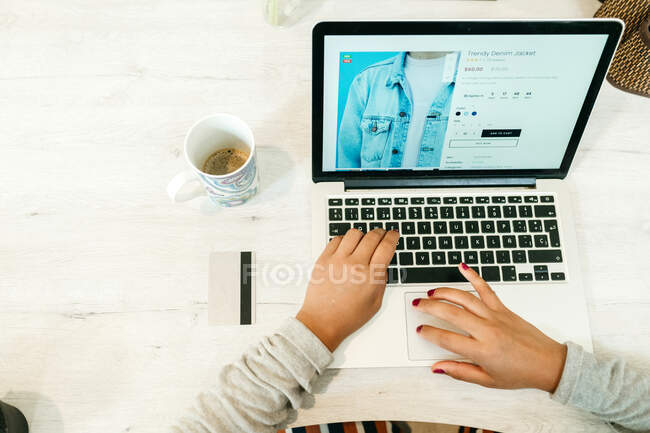 Сверху женщины используют нетбук во время онлайн-покупок, сидя за столом с пластиковой картой дома и выбирая товары — стоковое фото