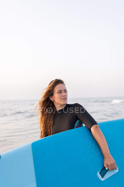 Female in swimsuit standing with SUP board in sea water in summer and looking away — Stock Photo