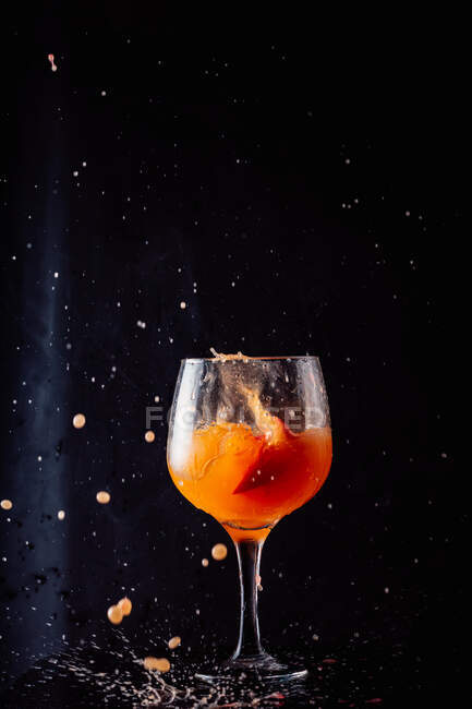 Kaltes alkoholoranges Getränk spritzt im Atelier aus Glaskelch auf schwarzem Hintergrund — Stockfoto