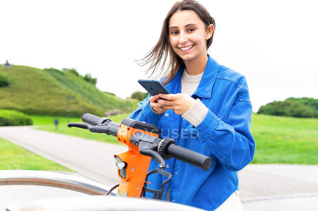 Conteúdo aluguer feminino estacionado scooter elétrico na cidade e navegação telefone móvel — Fotografia de Stock