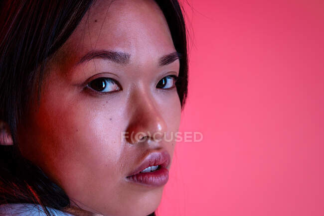 Primo piano di modello femminile etnico fiducioso in vestiti alla moda guardando la fotocamera in studio su sfondo rosa — Foto stock
