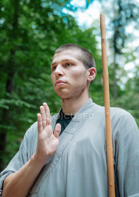 Низький кут нахилу людини з палицею тримає руку біля грудей, практикуючи кунг-фу в лісі — стокове фото