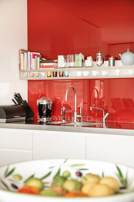 Дизайн интерьера современной домашней кухни с ярко-красным брызгом и посудой на полке над раковиной — стоковое фото