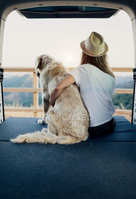 Unrecognizable female tourist embracing obedient Golden Retriever dog lying on mattress inside camper and admiring nature — Stock Photo