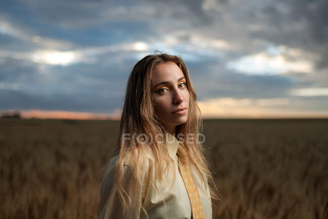 Young mindful female in formal wear with tie looking at camera among spikes in countryside — Stock Photo