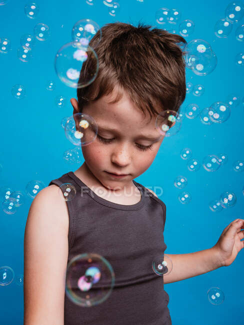 Мальчик-подросток, смотрящий в студии с мыльными пузырями на синем фоне — стоковое фото