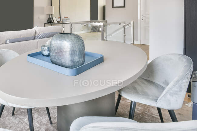 Стильний дизайн інтер'єру будинку зі зручними м'якими стільцями, розміщеними навколо овального столу з декоративною вазою в сучасній вітальні — стокове фото
