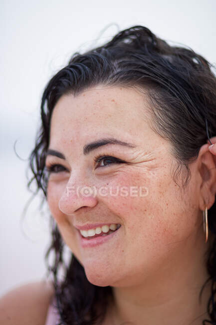 Sorridente femmina curvy regolazione bagnato capelli ondulati e guardando lontano su sfondo sfocato — Foto stock