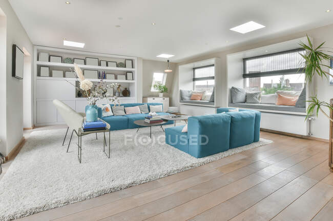 Design de interiores de espaço aberto sala de estar com sofá azul e cadeiras colocadas perto de pequena mesa em tapete macio em apartamento moderno com paredes brancas e teto iluminado com lâmpadas — Fotografia de Stock