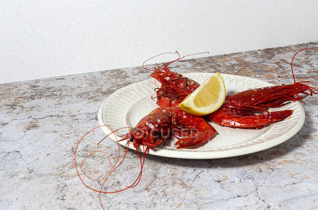 Sabroso marisco de camarones rojos cocidos con rodajas de limón fresco y sal gruesa sobre fondo blanco - foto de stock
