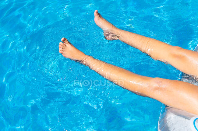 De cima da colheita pernas femininas anônimas deitadas no colchão inflável na piscina enquanto toma sol no dia ensolarado do verão — Fotografia de Stock