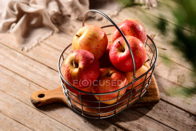 De cima de maçãs maduras saborosas em cesta de metal em tábua de corte no campo em dia ensolarado — Fotografia de Stock