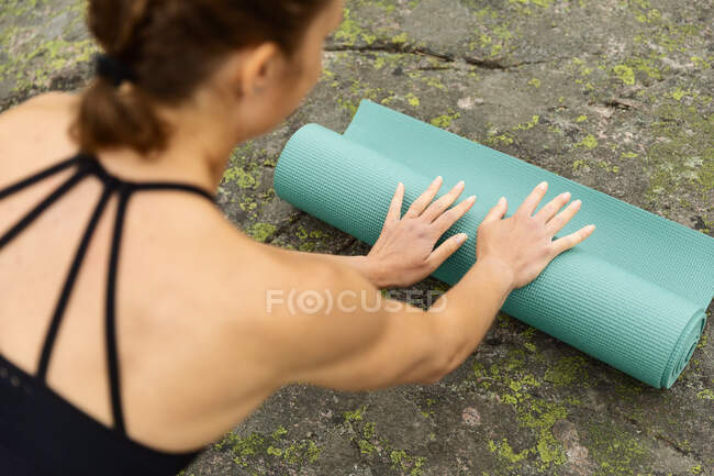 Back view woman in black activewear unrolling mat on rock at start of yoga session near swamp in nature — Stock Photo