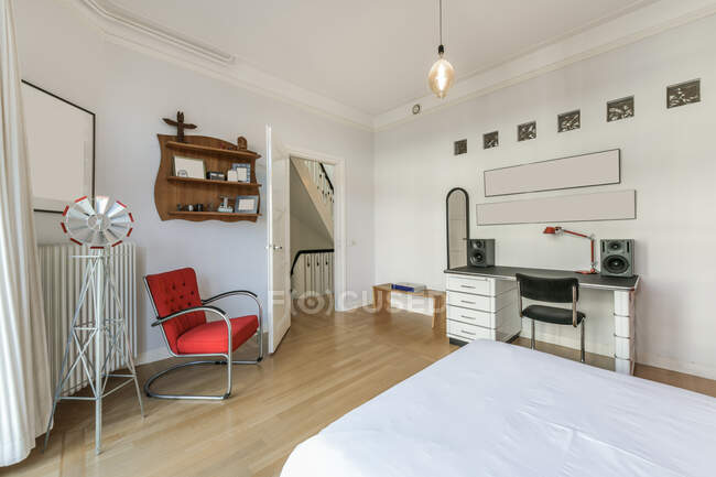 Moderno diseño interior de la casa de amplio dormitorio con gran ventana amueblada con cama y armario y sillón con lámpara de estilo loft - foto de stock
