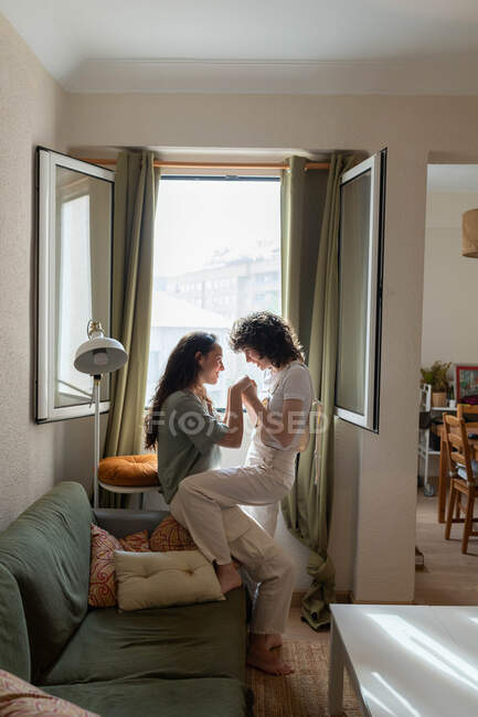 Visão lateral do conteúdo casal LGBT de mulheres apaixonadas no sofá em casa e olhando umas para as outras com amor — Fotografia de Stock