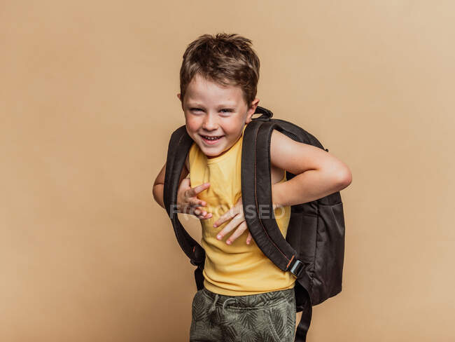 Positif cool écolier pré-adolescente avec sac à dos regardant la caméra sur fond brun en studio — Photo de stock