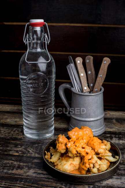 From above of delicious crispy chicken with cheese sauce placed on wooden table near glass bottle of water and utensils in restaurant — Stock Photo
