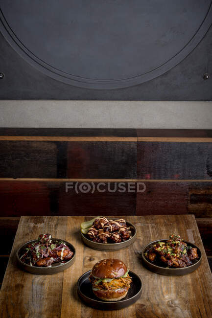 Сверху вкусный бургер с жареными булочками помещен рядом с тарелками с куриными крылышками в соусе барбекю в ресторане — стоковое фото