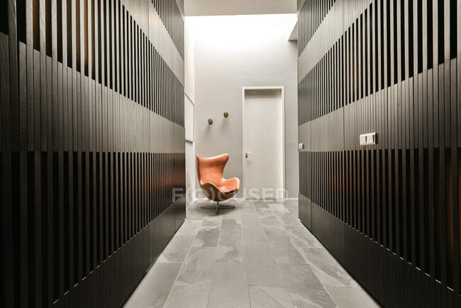 Vista prospectiva do interior do corredor com paredes listradas cinzentas e cadeira marrom colocada perto da porta de entrada — Fotografia de Stock