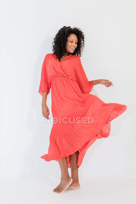 Sorrindo descalça mulher étnica com cabelo encaracolado em vestido da moda com ornamento listrado olhando para baixo — Fotografia de Stock