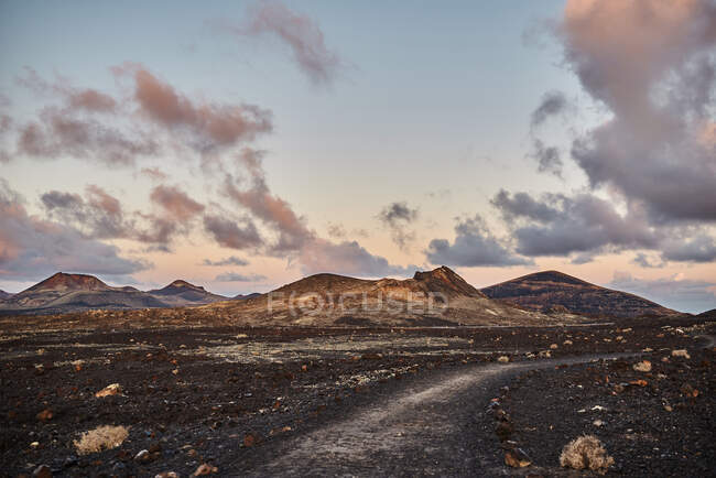 Schmale Straße durch trockenes Tal in der Nähe der Bergkette gegen wolkenverhangenen Himmel in Fuerteventura, Spanien — Stockfoto